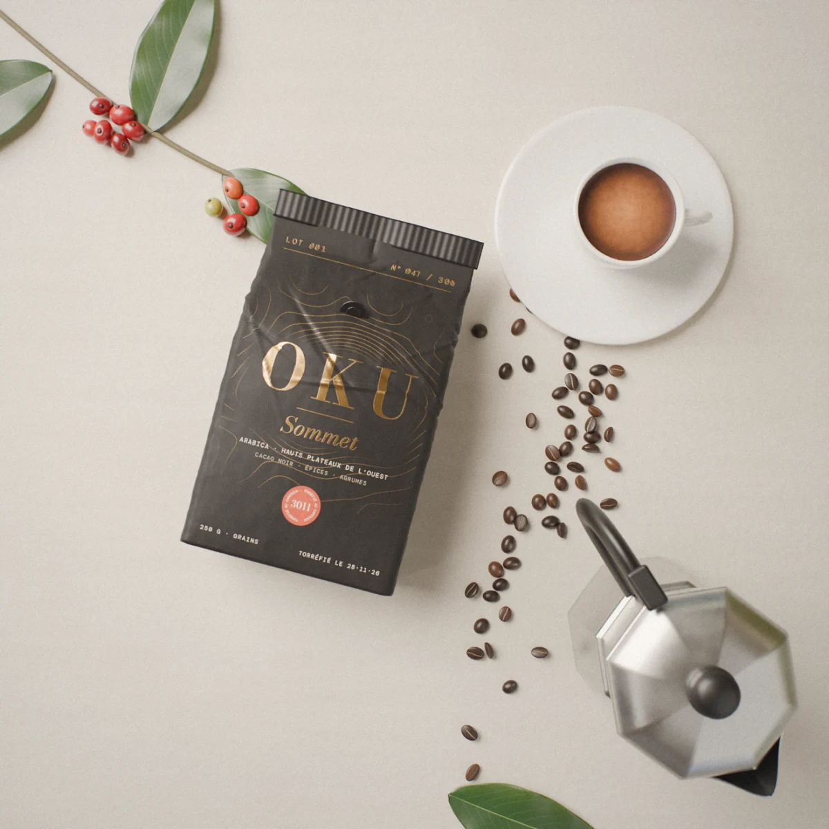 Sac OKU Sommet posé à plat sur une pierre claire, avec une tasse d'espresso, une cafetière italienne, des grains, une branche de caféier et ses cerises